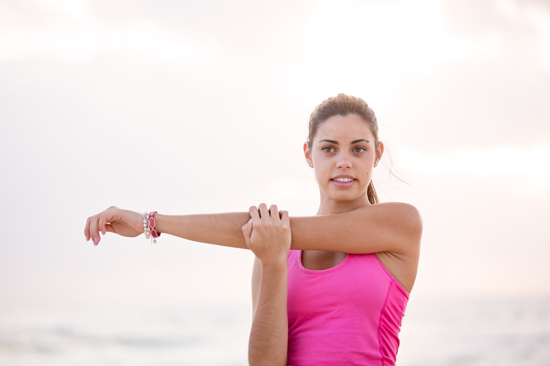 photography of woman in pink tank top stretching arm
